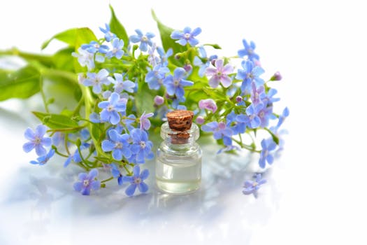 A glass bottle of essential oil beside delicate blue flowers, evoking calm and nature.